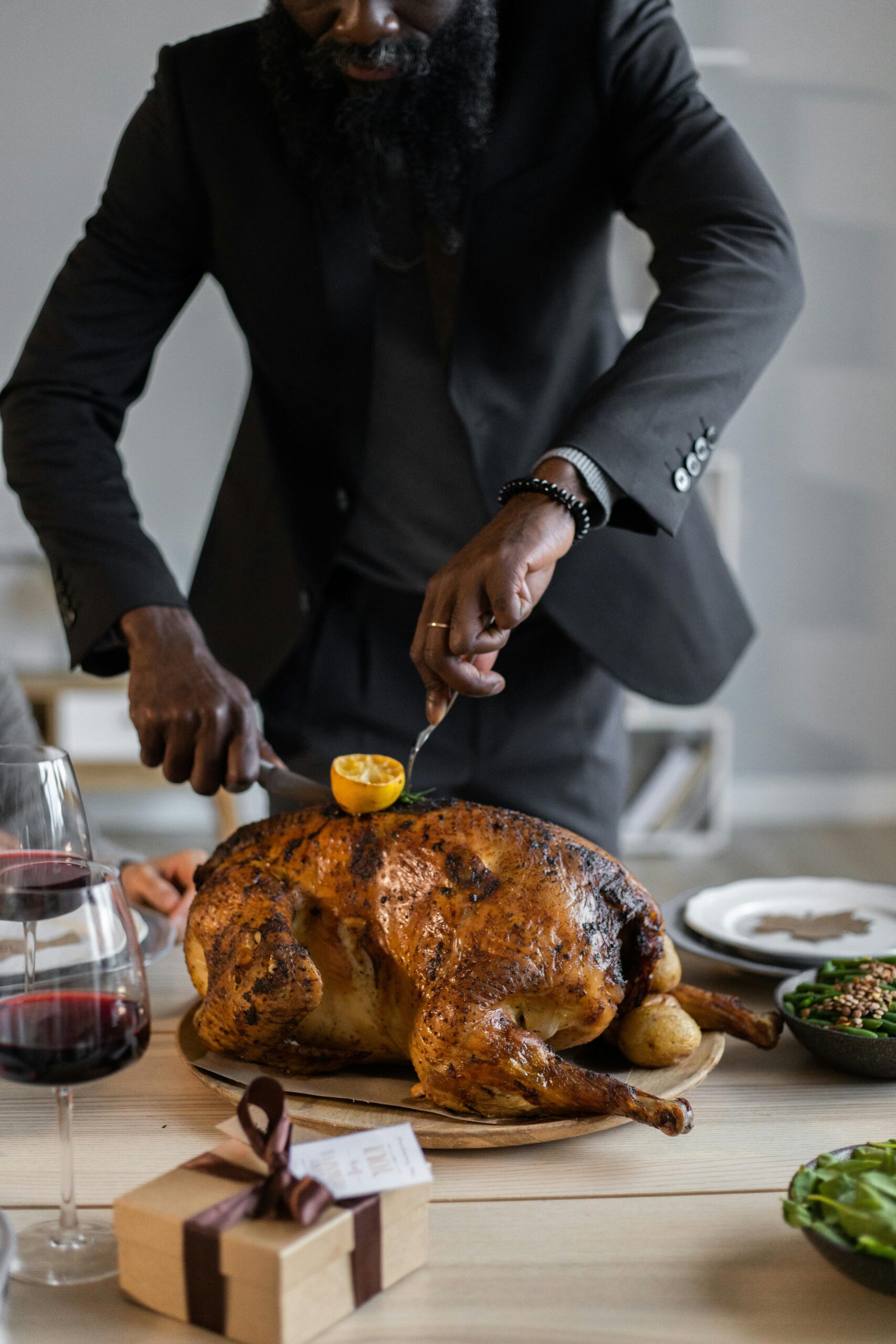 Crop unrecognizable bearded male in suit cutting roasted turkey in pieces with fork and knife while having Thanksgiving dinner